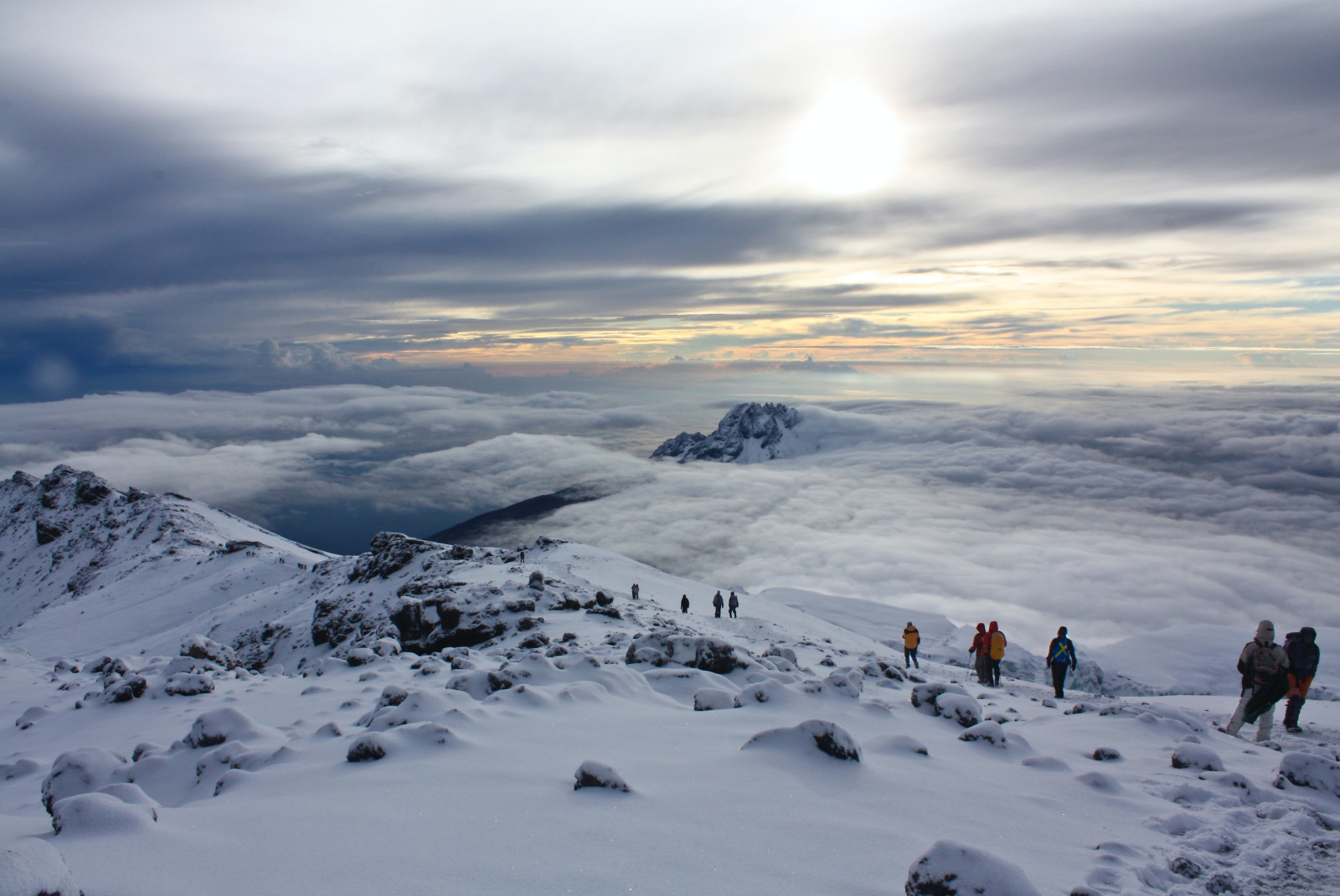 Ten hikers on top of Mount Kilimanjaro in Tanzania with white snow and and clouds and an orange sky
