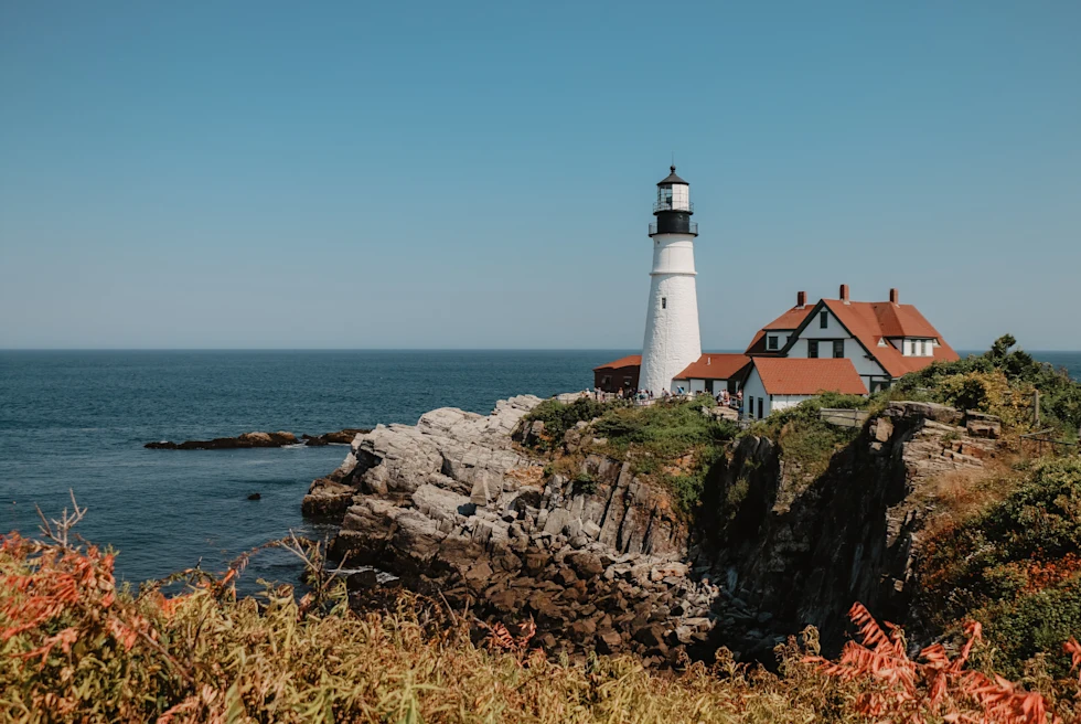 Body of water next to rocky cliff with white lighthouse during daytime