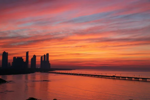 A golden, pink and lavender sunrise over Panama City, over the water and a silhouetted skyline.