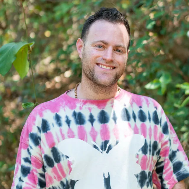 Travel Advisor Evan Freed with a pink tie-dye butterfly shirt in front of trees.