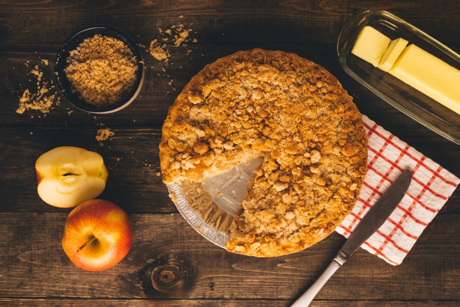 Apple pie on a brown table with apples, brown sugar and butter on the side. 