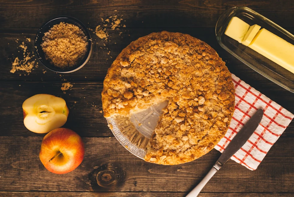 Apple pie on a brown table with apples, brown sugar and butter on the side.