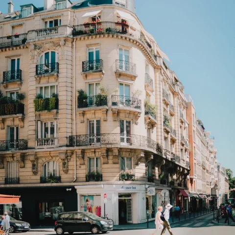 Two people walking on the street next to a tall building on a sunny day