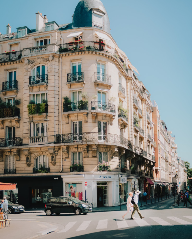 Two people walking on the street next to a tall building on a sunny day