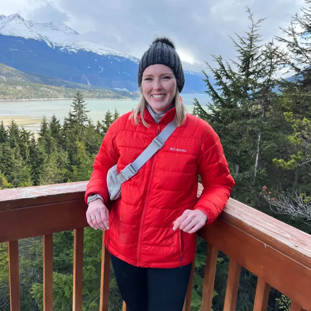 Travel Advisor emily keeton wears a red jacket and gray snow hat standing on a wood porch in a snowy mountain range