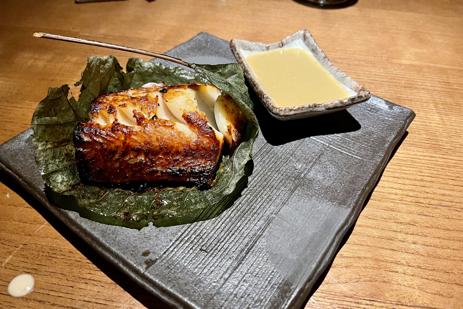 Fish and a saucer filled with sauce on black plate on wooden table
