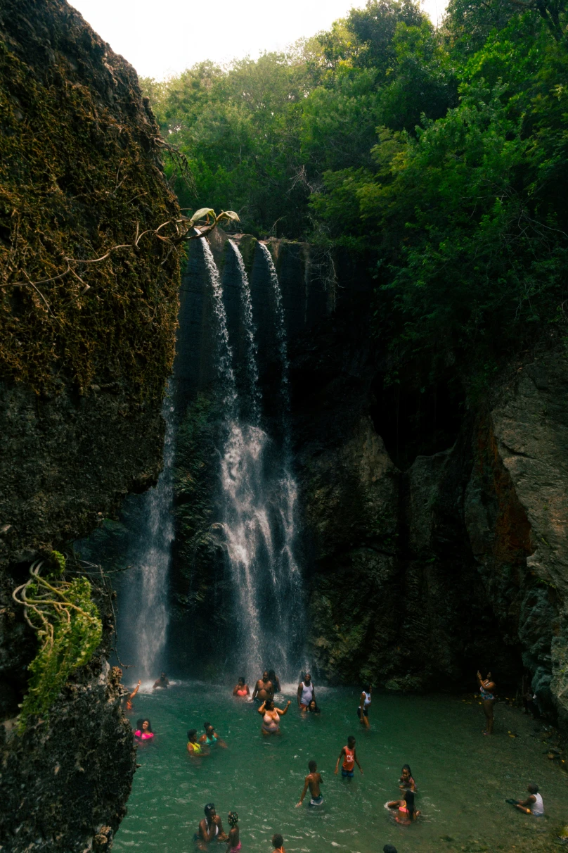 People in a body of water at the bottom of a waterfall