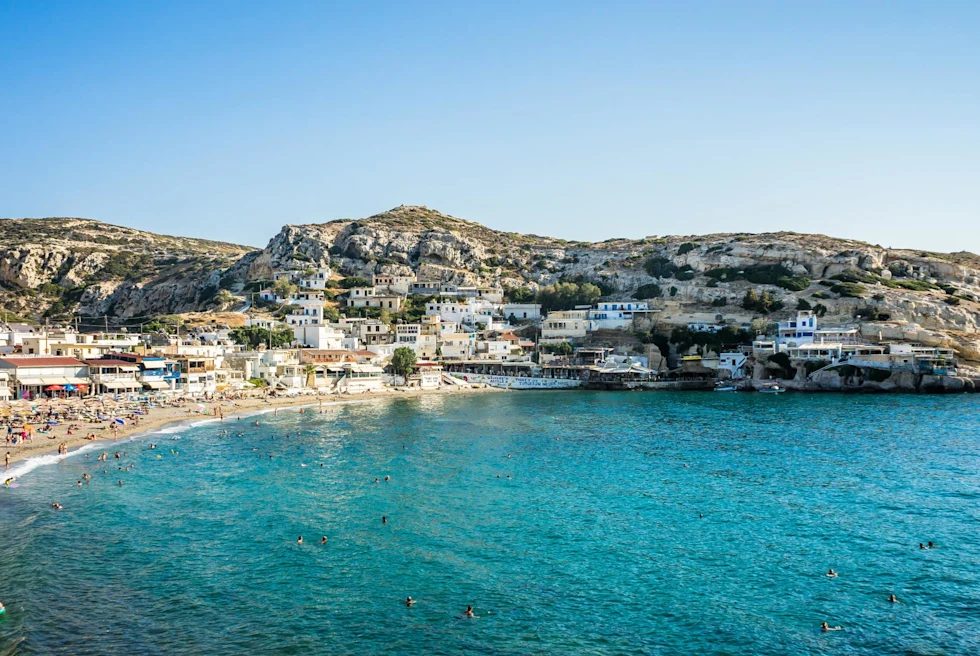 busy beach with clear blue waters off sloping rocky island city