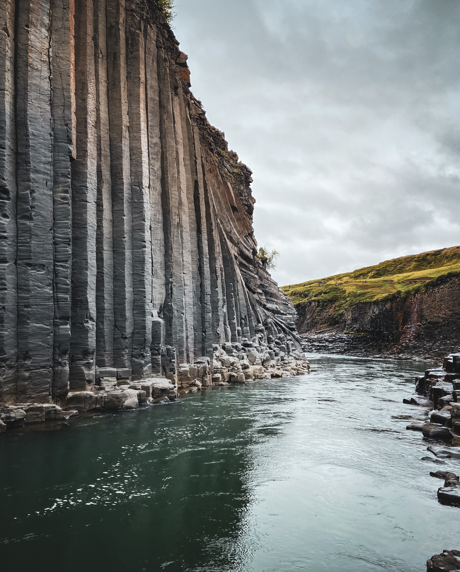 A grey stone cliff in Iceland with a green emerald river flowing through.