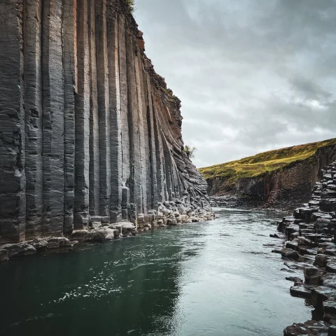 A grey stone cliff in Iceland with a green emerald river flowing through.
