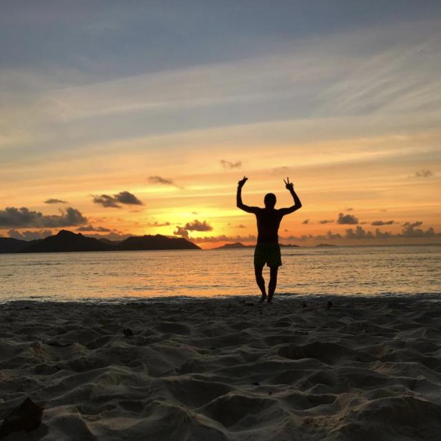 Person posing on the beach in front of colorful sunset