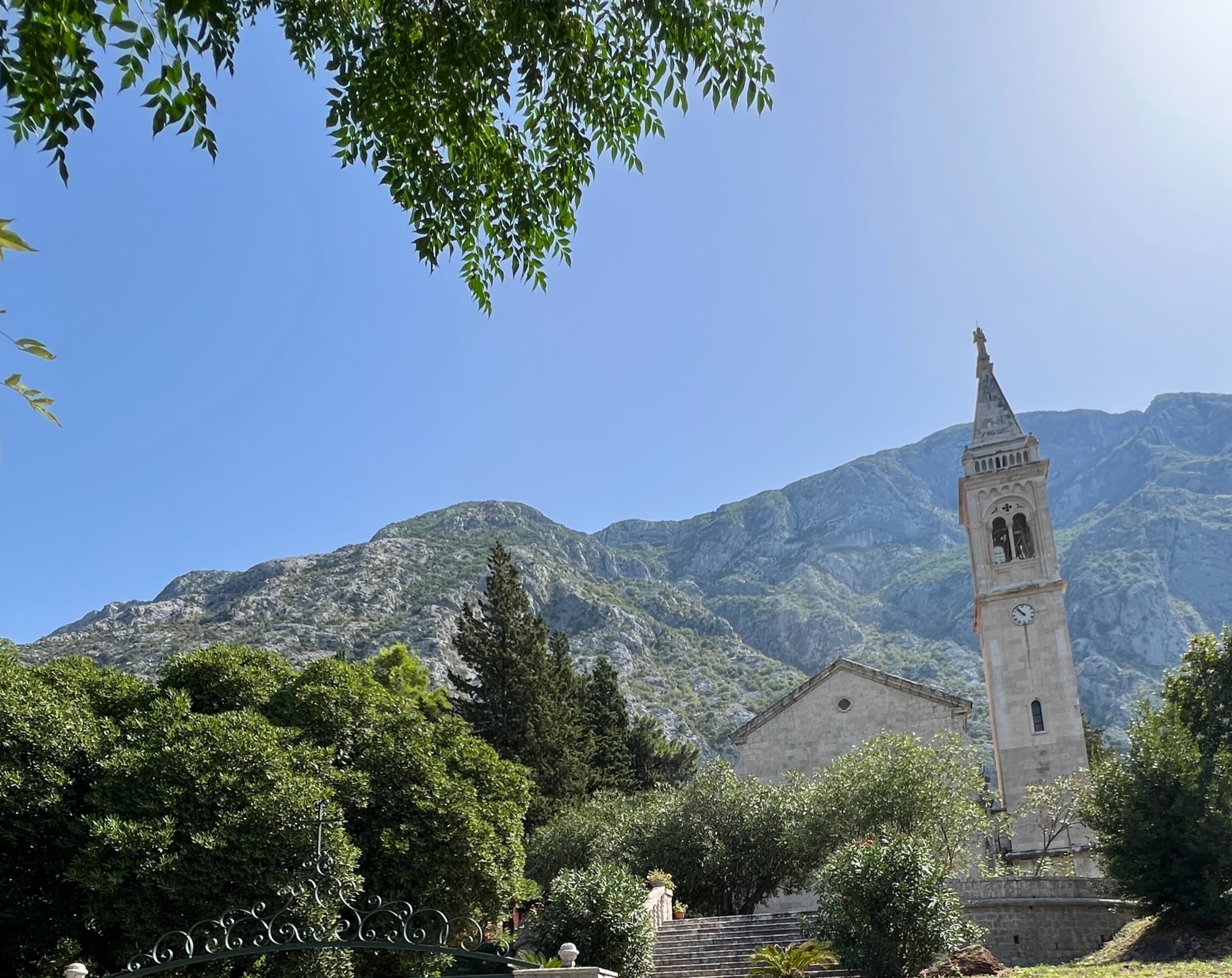 a steeple of a church in front of a green mountain range on a sunny day