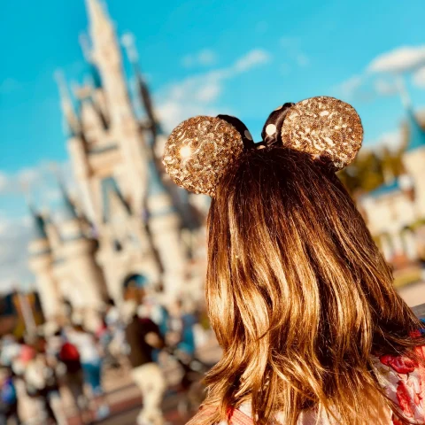 A woman wearing golden Mickey Ears at Disneyland with the castle blurred out in the background.
