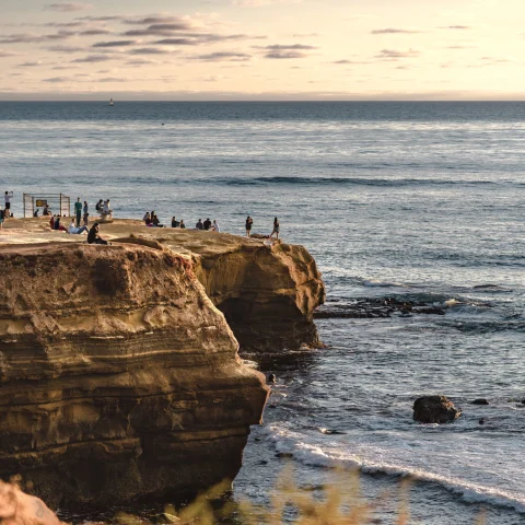 people stand on the cliffs over the ocean at sunset