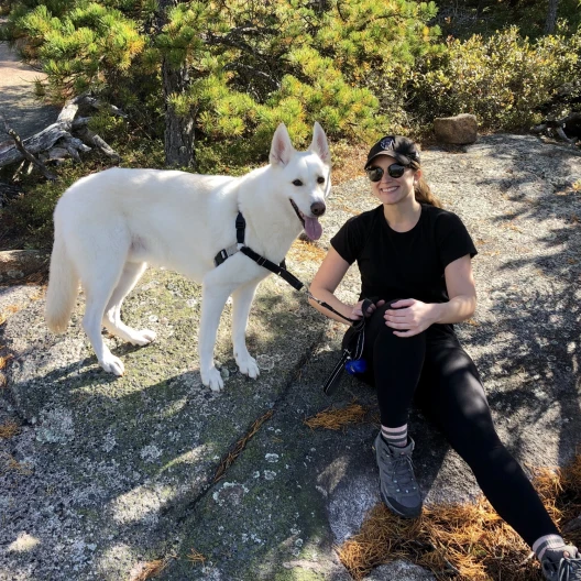 Travel advisor Hollie Grantham sits near a white dog on a mountain trail