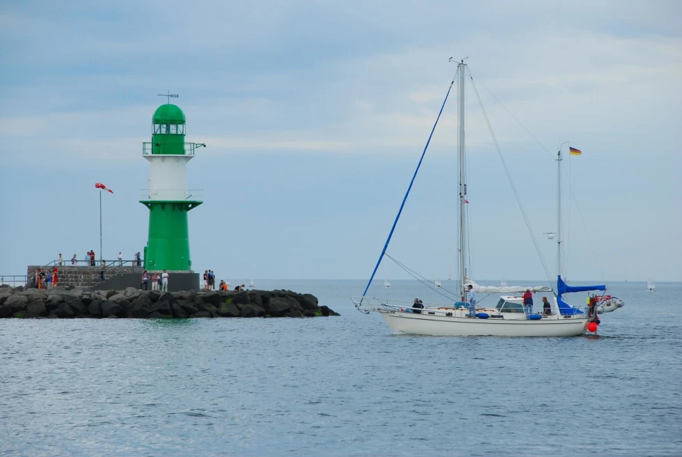 green lighthouse on a small island and a sailboat moored nearby with the sails down