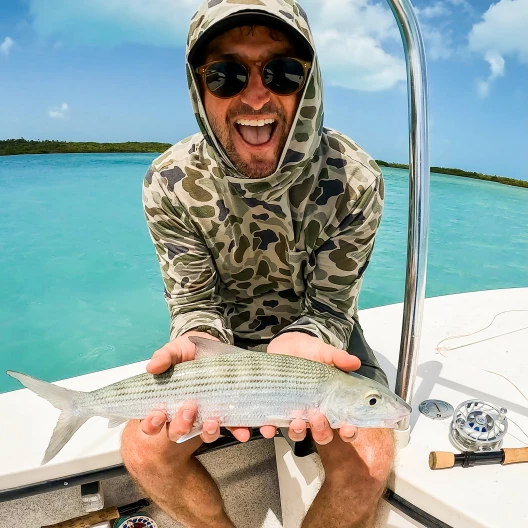 Travel Advisor Ian White in front of blue water holding a fish.