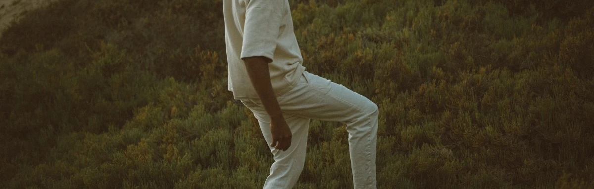 Man walks up an unpaved hill through grass and shrubs.