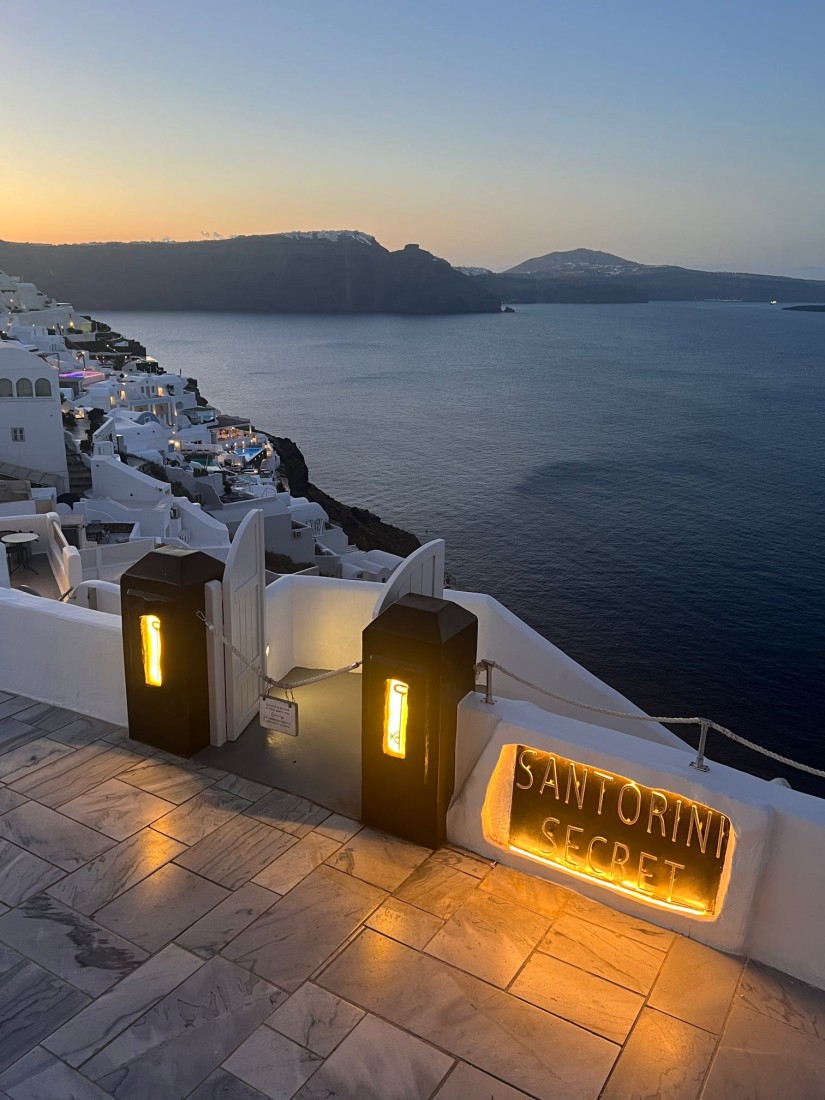 A view of the caldera in Santorini with white buildings and an ocean view at sunset