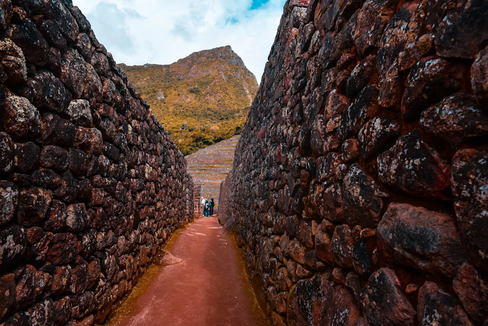 Red and brown stone walls with large mountains in the background at Machu Picchu in Peru.