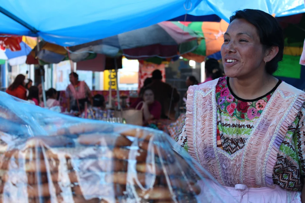 A woman wearing a colorful shirt and pink apron at a food stall with cookies
