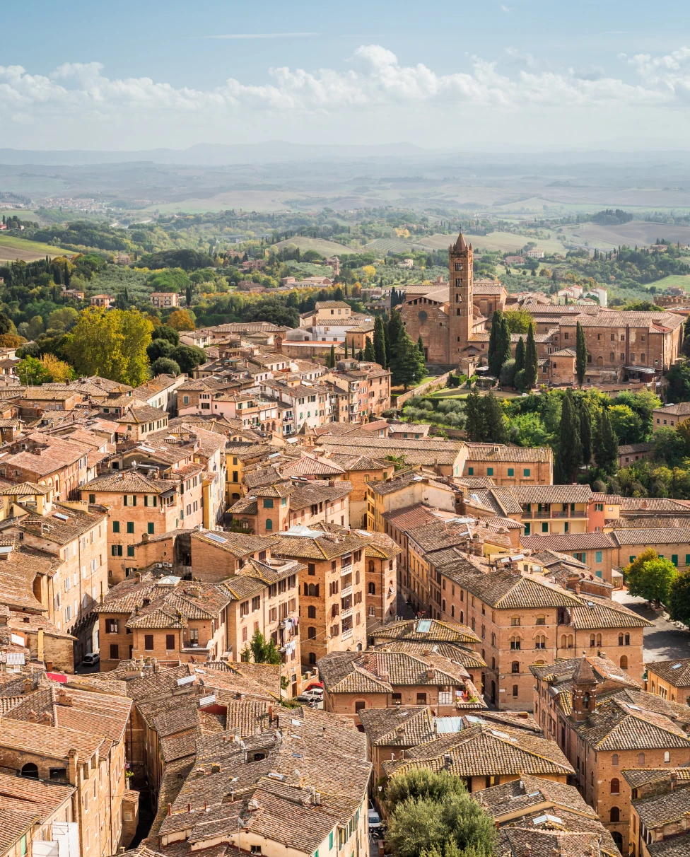 The tan and orange colorful town of Lucca with green trees immersed throughout in Tuscany, Italy.