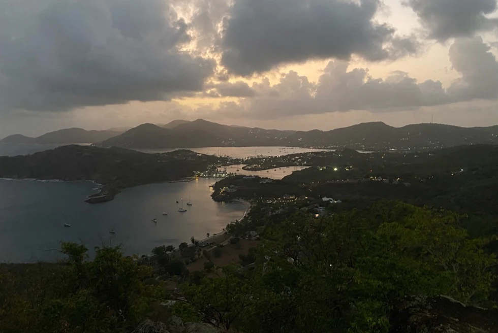 sun sets over an island as the harbor lights up below
