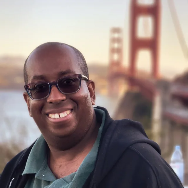Travel Advisor Jason Byrd in a green shirt, black sweatshirt in front of the San Francisco bridge.