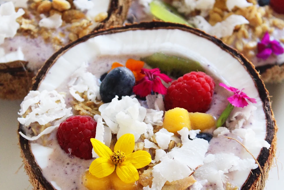 Acai topped with fruit and flowers served in a coconut