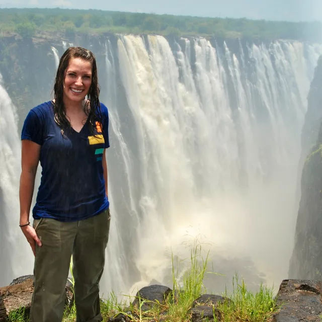 Travel advisor Carole Hansen wearing blue T-short, standing on a mountain and a waterfall in the background.