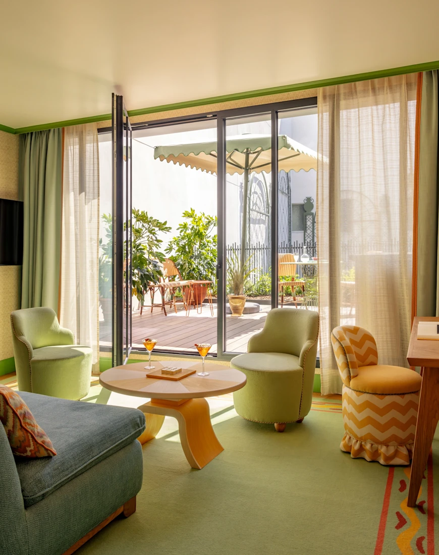 a luxe, colorful living room with a green carpet and blue and orange furniture overlooks a sunny terrace