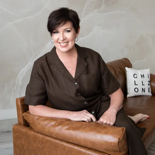 Travel Advisor Kelly Moore sitting on a camel brown sofa in dark brown clothes. 