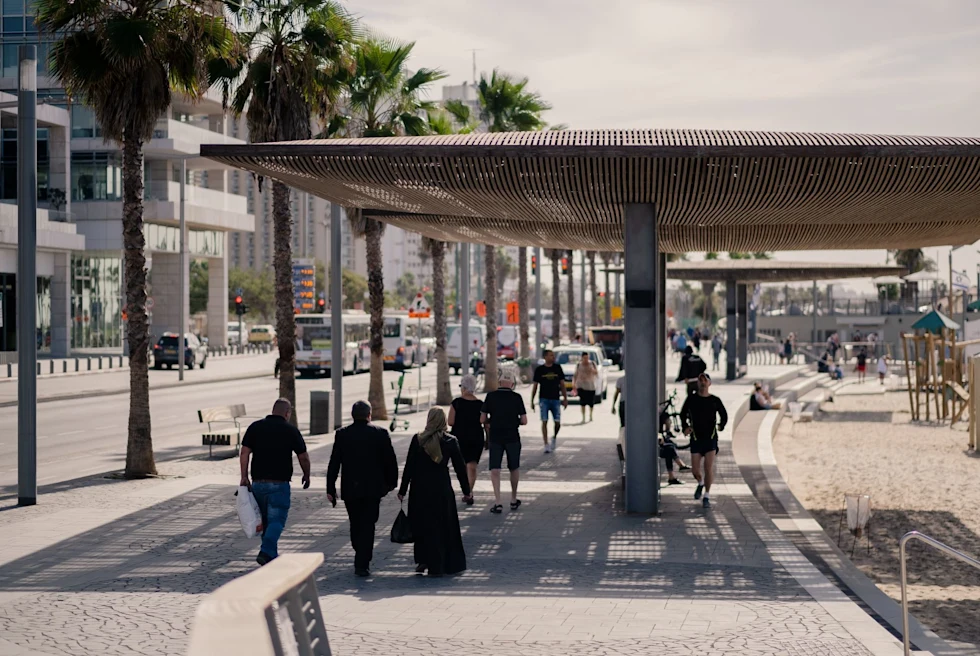 people walking on the sidewalk next to a beach