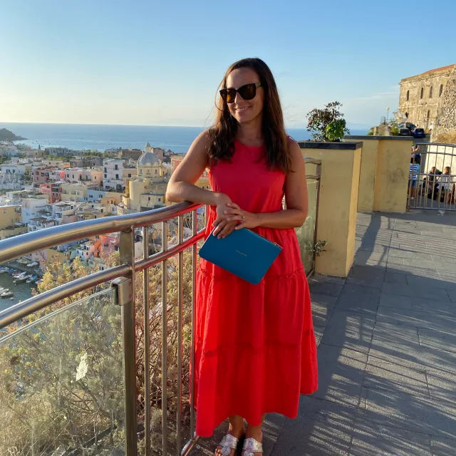 Ashley in a red dress standing on a balcony overlooking a coastal town