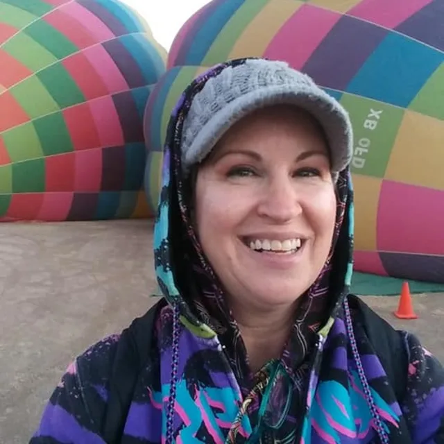 Travel advisor Elisa Goad in a purple and blue hoodie in front of colorful hot air balloons.