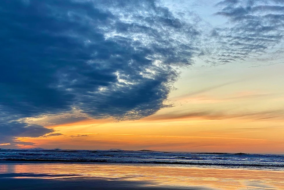 orange, yellow and blue sunset over beach reflects on the wet sand