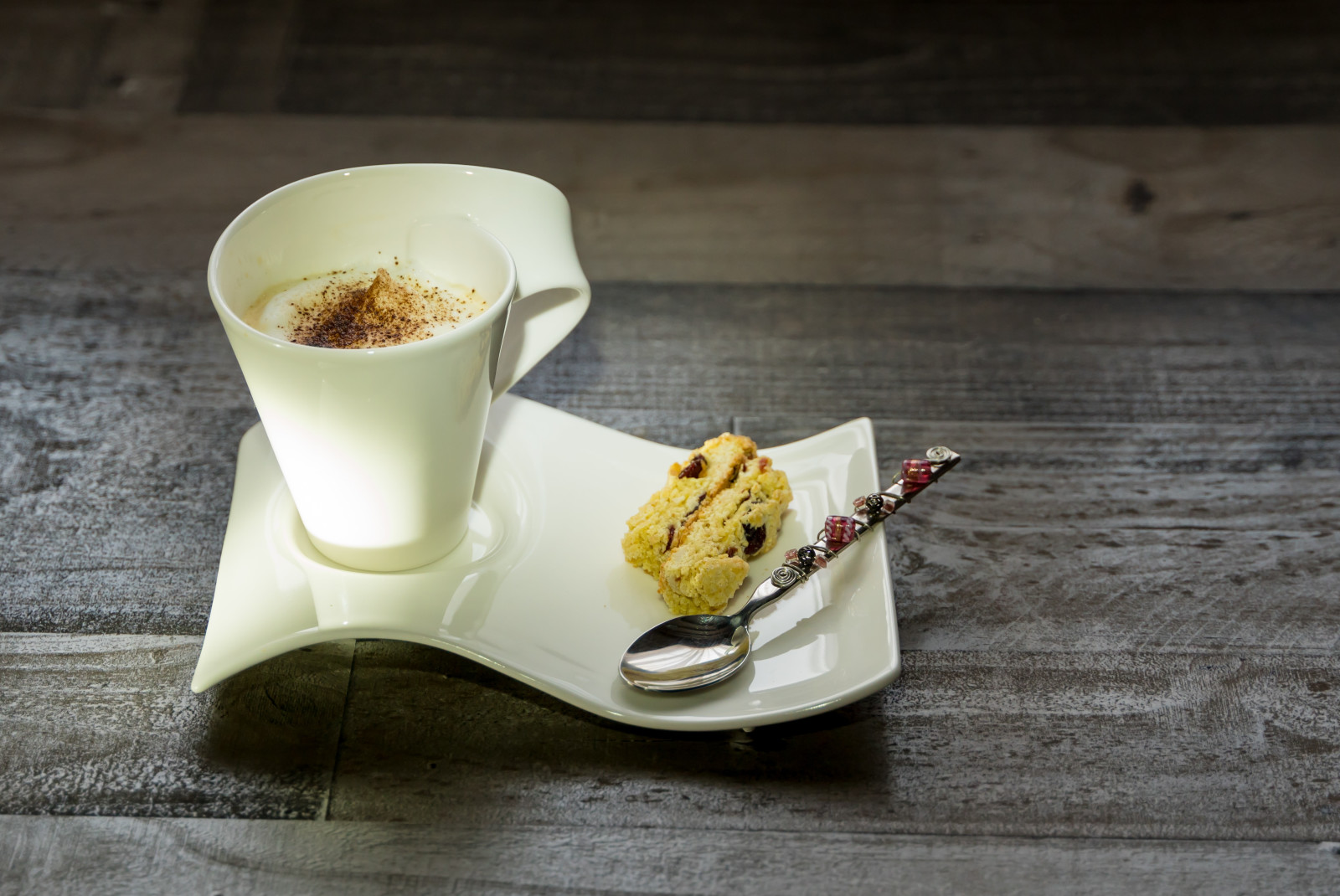 A coffee and biscotti in white cutlery on a brown table.