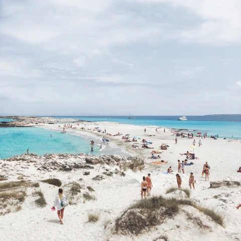 People walking on white sand beach next to blue water on a cloudy day