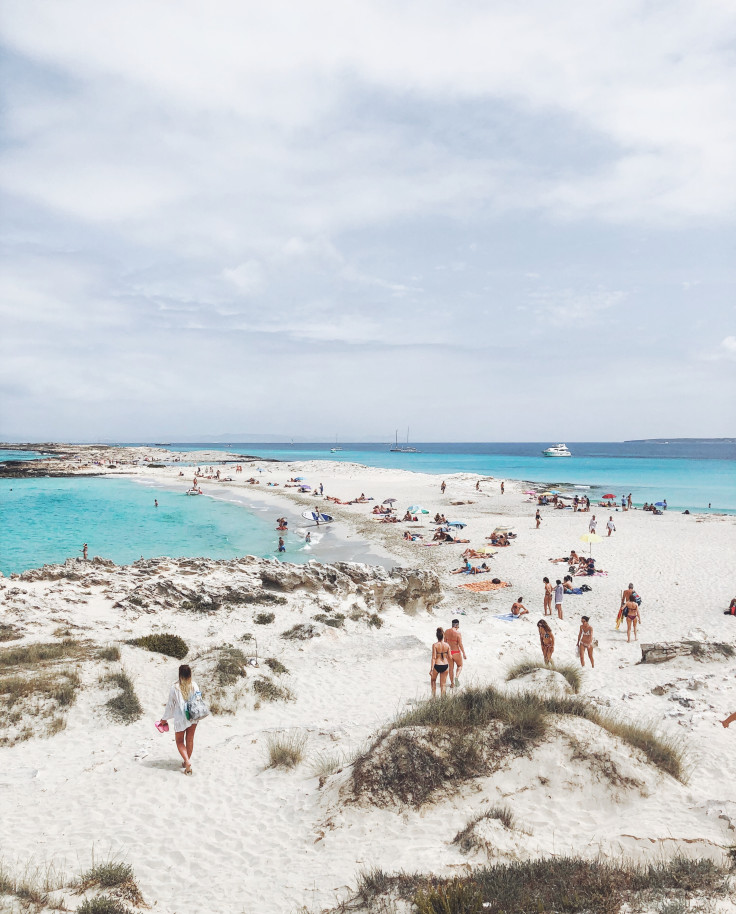 People walking on white sand beach next to blue water on a cloudy day