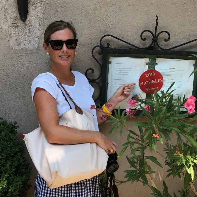 Travel Advisor Maria Moore in a white shirt pointing at a Michelin sticker on a menu.