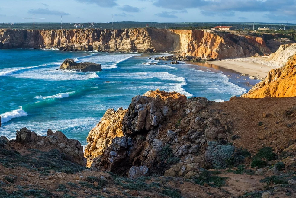 vista of a rocky beach surrounded by cliffs with waves crashing on a sandy shore