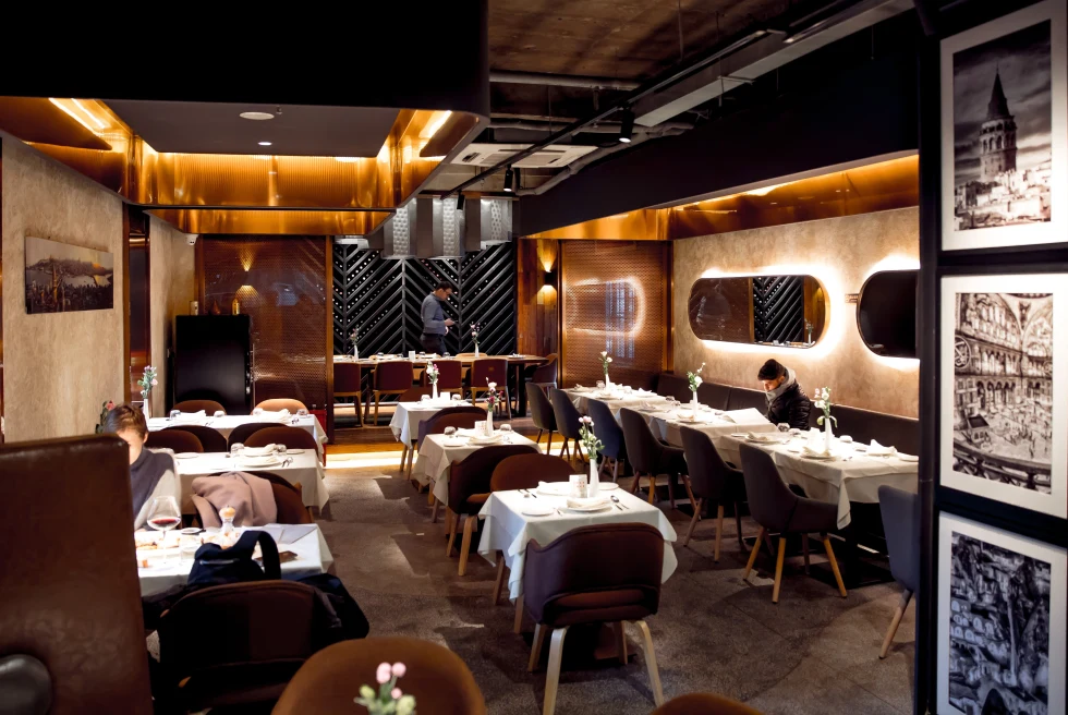 Inside of a restaurant with dark brown chairs and white table clothes. 