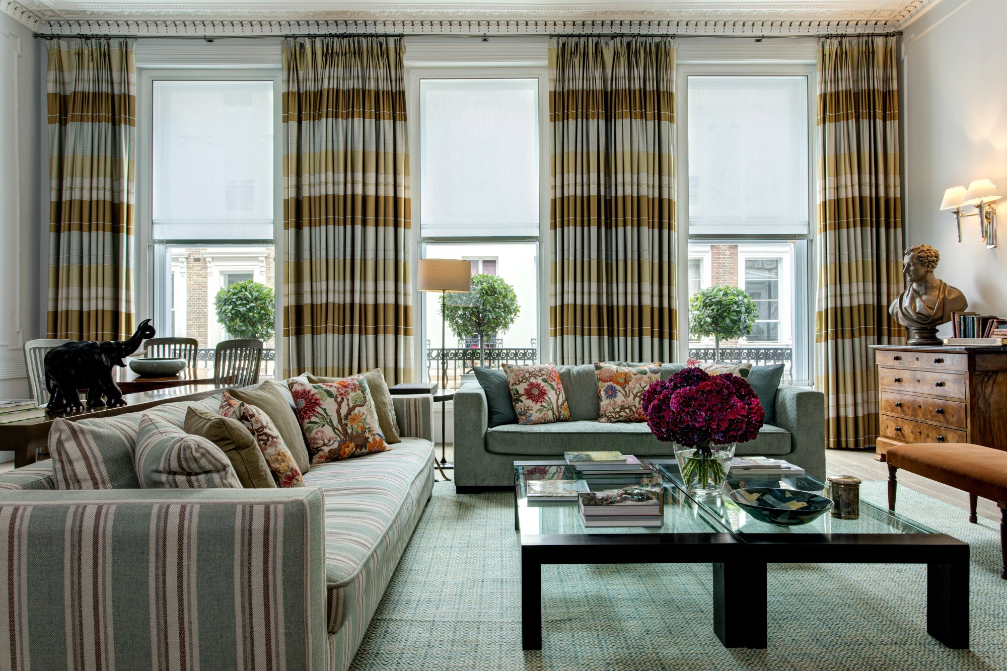 a swanky living room with two large blue couches surrounding a coffee table decorated with a vase of red roses