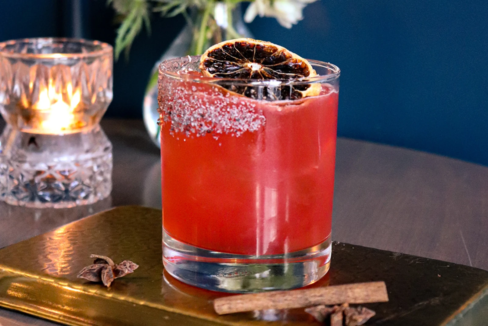 Red drink in clear glass with cinnamon clove salt rim and dried orange on gold tray in Mexico