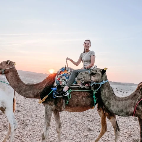 A lady sitting on a camel during sunset.