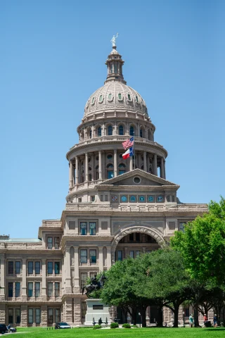 Capitol building with grass and flags with blue sky in Austin, Texas