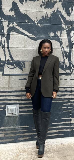 Fora travel agent Samaria Leonard wearing blazer standing in front of blue and grey wall