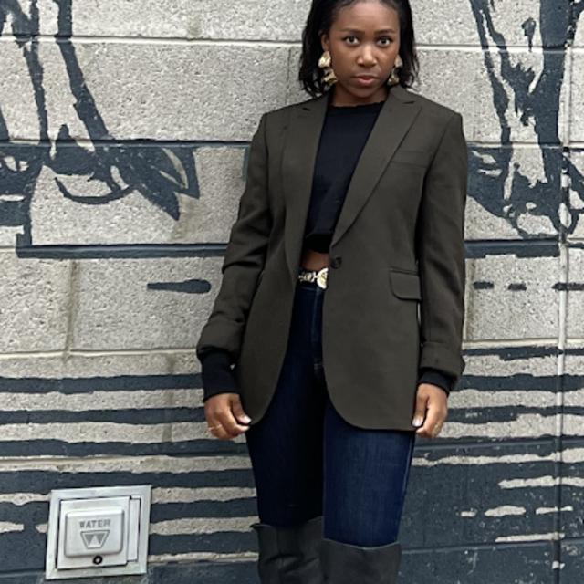 Fora travel agent Samaria Leonard wearing blazer standing in front of blue and grey wall