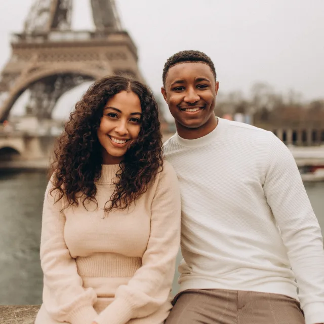 Travel Advisor Esrie Crawford sits on a ledge in front of the Eiffel Tower wearing a cream colored dress next to her husband