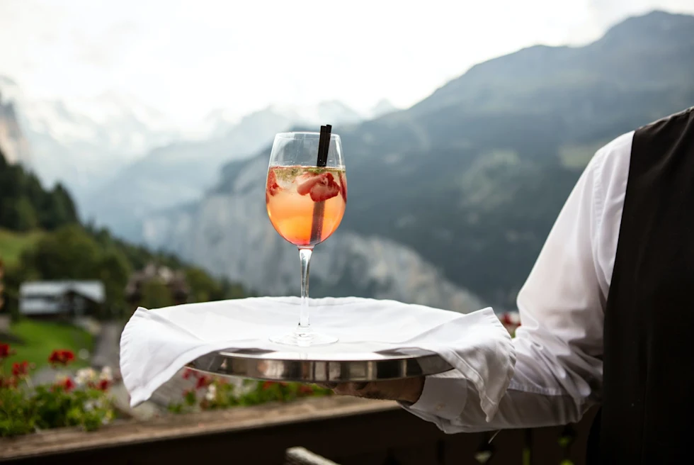 A waiter carrying a wine glass on a tray with snow clad mountains in the background.